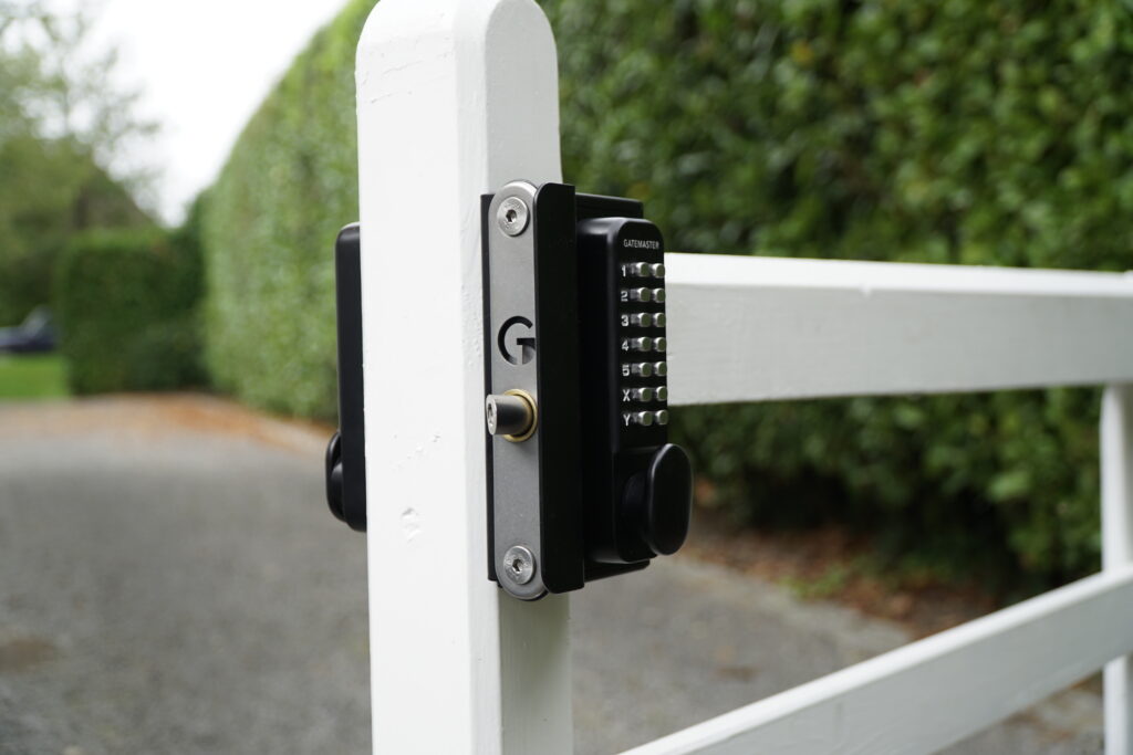 gate lock with code on white wooden fence in front of green hedge and paved drive